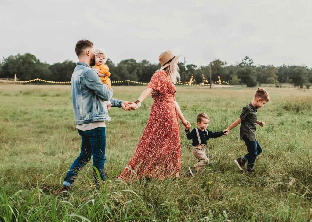 A family of five walks hand in hand through a grassy field, as if leaving a family office meeting behind for quality time together. The casually dressed parents and their three young children enjoy the outdoors, framed by trees in the background.